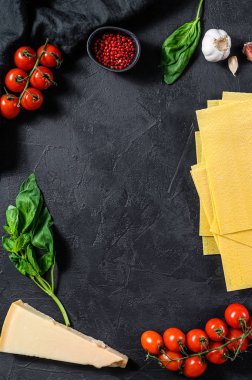 Lazanya pişirme konsepti. Malzemeler, lazanya, fesleğen, vişneli domates, parmesan, sarımsak, biber. Siyah arka plan. Üst Manzara. Metin için boşluk