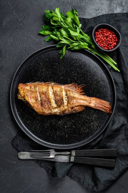 Yuvarlak bir tabakta maydanozla servis edilen deniz levreği. Siyah arka plan. Üst Manzara. Metin için boşluk