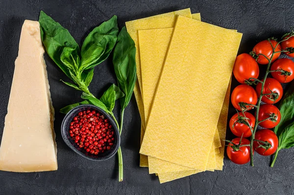 El concepto de cocinar lasaña. Ingredientes, hojas de lasaña, albahaca, tomates cherry, parmesano, ajo, pimienta. Fondo negro. Vista superior — Foto de Stock