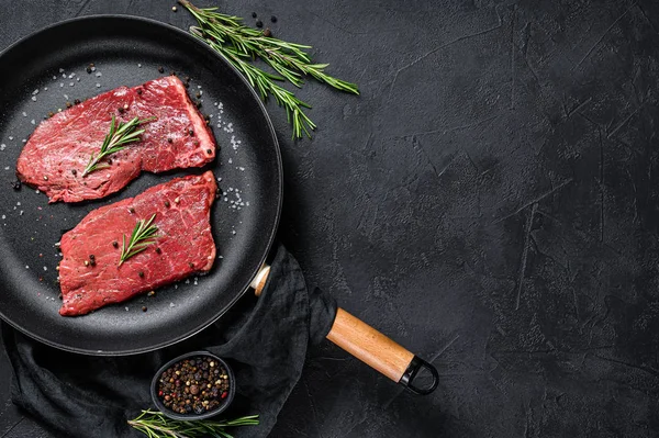 Bife de lombo cru numa frigideira. Carne de vaca. Fundo preto. Vista superior. Espaço para texto — Fotografia de Stock