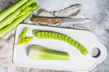 Beyaz tahta keserken dilimlenmiş taze kereviz sapı. Gri arka plan. Üst görünüm