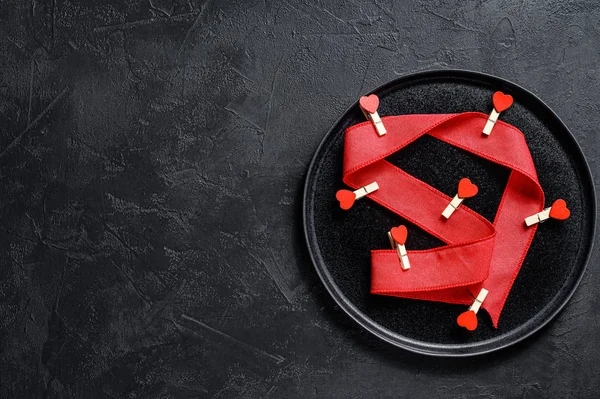 Valentijnsdag tafelschikking met rood lint en hartjes. Zwarte achtergrond. Bovenaanzicht. Ruimte voor tekst. — Stockfoto