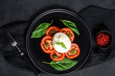 Siyah tabakta servis edilen Burrata peyniri ve domates salatası. Karanlık arka plan. Üst görünüm
