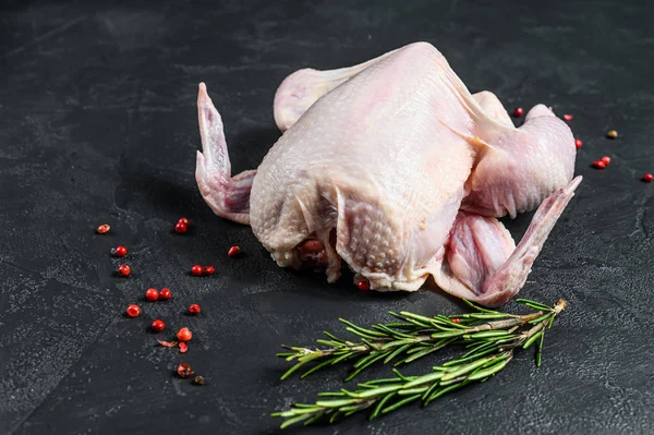 Raw whole chicken with rosemary and pink pepper. Black background. Top view