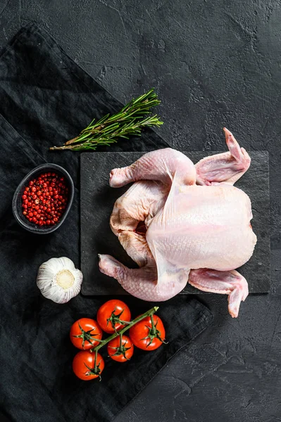 Raw whole chicken with rosemary and pink pepper. Black background. Top view. Space for text