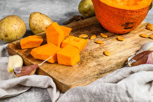 Ingredients for pumpkin soup. Pumpkin pieces on a cutting Board. Cream soup. Gray background. Vegetarian cuisine