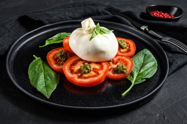 Siyah tabakta servis edilen Burrata peyniri ve domates salatası. Karanlık arka plan. Üst görünüm