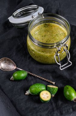 Cam kavanozdaki tahta kesme tahtasındaki yeşil fayjoa reçeli. Doğal ev yapımı tatlı. Siyah arka plan. Üst görünüm