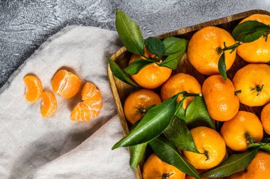 Ahşap bir kasede yaprakları olan taze mandalina ve portakal. Gri arka plan. Üst görünüm