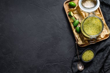 Cam kavanozdaki tahta kesme tahtasındaki yeşil fayjoa reçeli. Siyah arka plan. Üst Manzara. Metin için boşluk