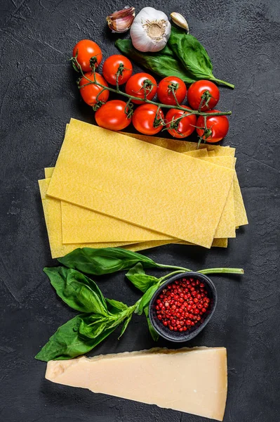 Fogli di lasagne crude. Ingredienti Basilico, pomodorini, parmigiano, aglio, pepe. Fondo nero. Vista dall'alto — Foto Stock