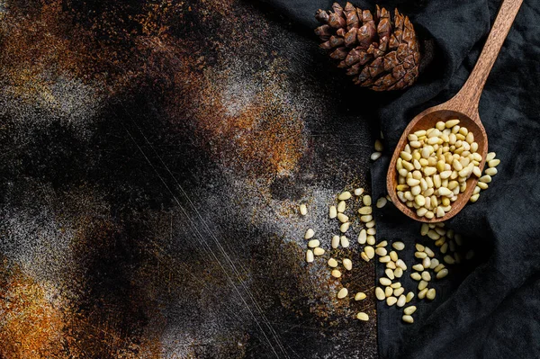 Pinoli nel cucchiaio e pigna. Cibo biologico. Fondo nero. Vista dall'alto. Spazio per testo — Foto Stock