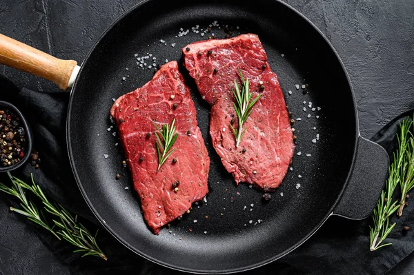 Rauwe biefstuk van biefstuk in een koekenpan. Rundvlees. Zwarte achtergrond. Bovenaanzicht — Stockfoto
