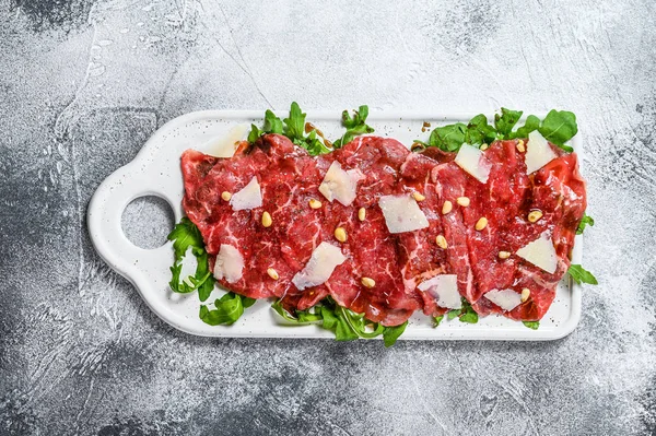 Black angus beef carpaccio with parmesan cheese. Gray background. Top view