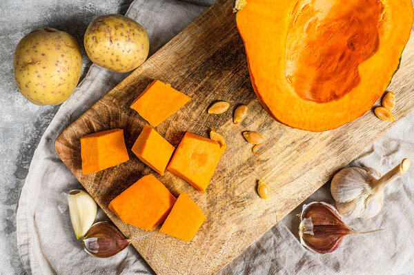 The concept of cooking pumpkin soup. Pumpkin pieces, potatoes, garlic, pumpkin seeds. Cream soup. Gray background. Vegetarian cuisine