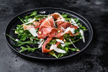 Serrano jamon, jambon, roka ve parmesan peynirli salata. Siyah arkaplan, üst görünüm.