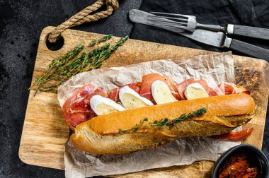 Jambonlu sandviç, dilimleme tahtasındaki peynirli peynirli sandviç. Siyah arkaplan, üst görünüm.