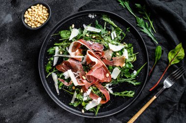 Parmalı salata, jambon, roka ve parmesan peyniri. Siyah arkaplan, üst görünüm.