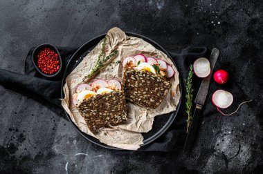 Sıcak somon, yumurta ve turplu tahıllı ekmeğin tostu. Siyah arkaplan, üst görünüm.