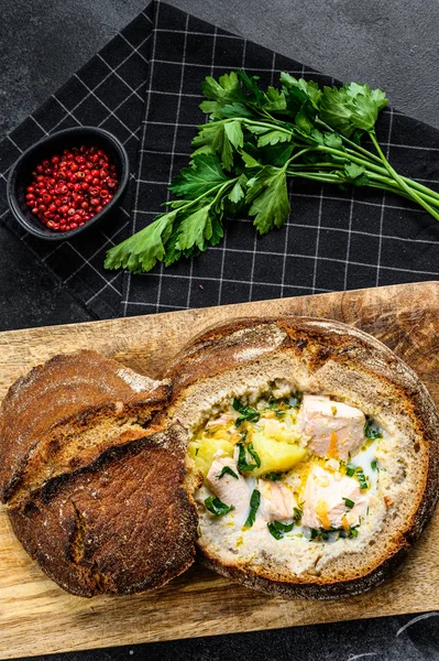 Финский кремовый рыбный суп с лососем, форелью, картофелем, подаваемый в хлебе. Черный фон, вид сверху. — стоковое фото