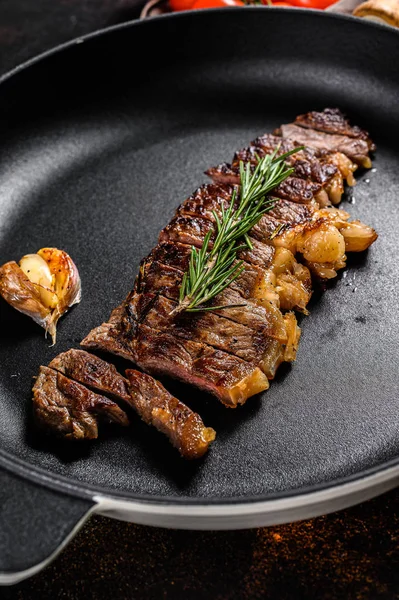 Beef New York strip steak in a frying pan. Space for text. Marble premium beef. Dark background