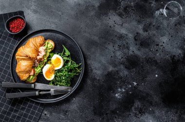 Sıcak somon füme kruvasan, avacado, roka ve yumurta. Siyah arka plan. Üst Manzara. Metin için boşluk