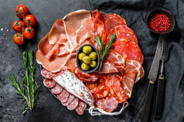 Geleneksel İspanyol mezelerinden yapılmış bir tabak et. Chorizo, Jamon Serrano, Lomo ve Fuet. Siyah arka plan. Üst görünüm.