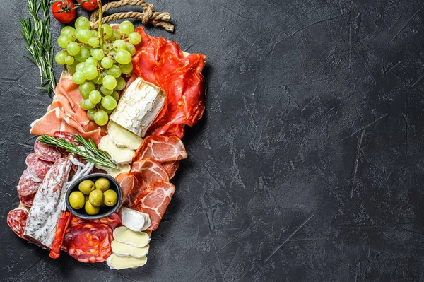 Antipasto piatto di carne fredda con uva, prosciutto, fette di prosciutto, carne essiccata di manzo, salame chorizo, fuet, Camembert e formaggio di capra. Fondo nero. Vista dall'alto. Copia spazio — Foto Stock