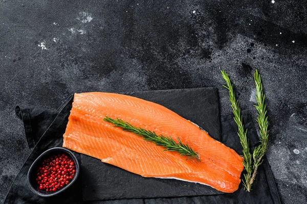 Raw trout fillet with rosemary and pink pepper. Organic fish. Black background. Top view. Copy space