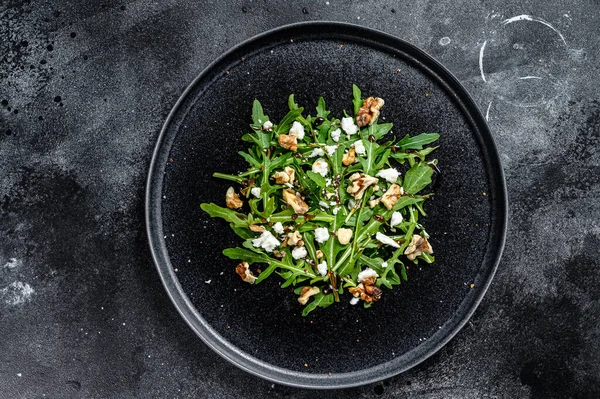 Healthy salad with arugula, goat cheese, nuts and vinaigrette sauce. Black background. Top view.