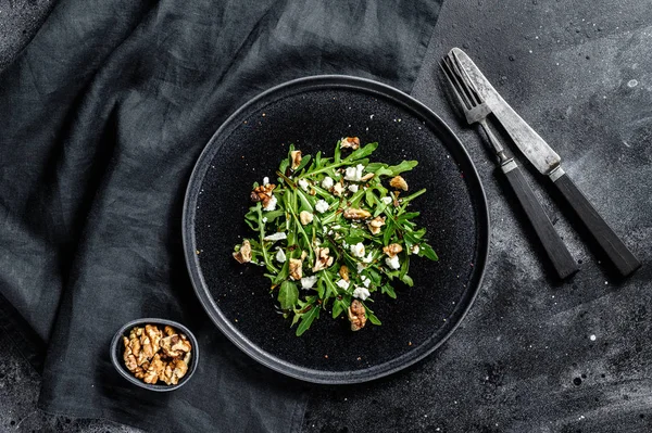 Healthy salad with arugula, goat cheese, nuts and vinaigrette sauce. Black background. Top view.