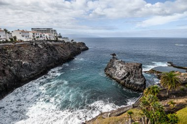 Siyah kayalar, oteller ve Atlantik Okyanusu ile volkanik sahilin manzarası. Seçici odaklanma. 20.01.2020 Los Gigantes, Tenerife.