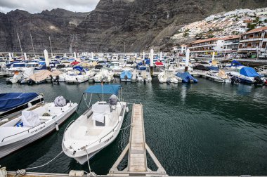 Volkanik dağların arkasındaki limanda yatlar ve botlar. Seçici odaklanma. 20.01.2020 Los Gigantes, Tenerife.