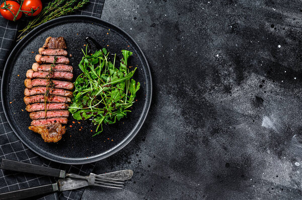 Sliced sirloin steak, marbled beef meat with arugula. Black background. Top view. Copy space.