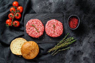Hamburger pişirmek için gerekli malzemeler. Kıymalı börek, çörek, domates, otlar ve baharatlar. Siyah arka plan. Üst görünüm.