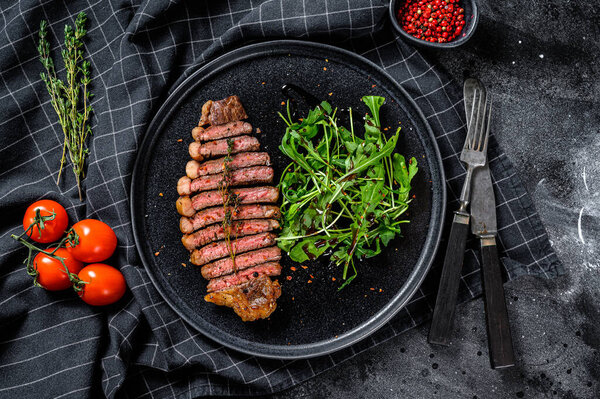 Fillet entrecote steak, marbled beef meat with arugula. Black background. Top view.