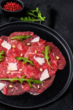 Siyah tabakta sığır eti, parmesan sosu, peynir ve roka. Siyah arka plan. Üst görünüm.