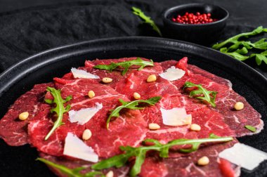 Arugula ve parmesan peynirli mermer sığır carpaccio. Siyah arka plan. Üst görünüm.