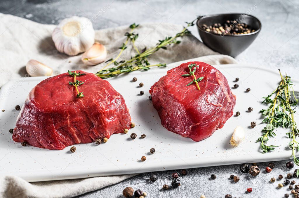 Raw filet Mignon steak on a white chopping Board. Beef tenderloin. Gray background. Top view.