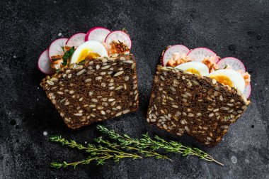 Sıcak somon, yumurta ve turplu tahıllı ekmeğin tostu. Siyah arkaplan, üst görünüm