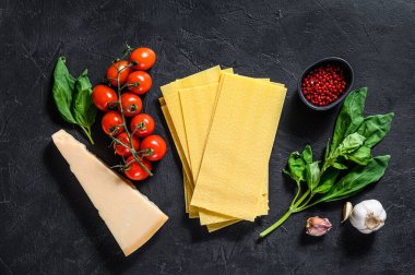 Lazanya pişirme konsepti. Malzemeler, lazanya, fesleğen, vişneli domates, parmesan, sarımsak, biber. Siyah arka plan. Üst görünüm.