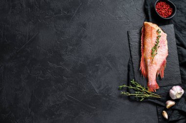 Kekikle taş bir tahtada çiğ kırmızı deniz levreği. Siyah arka plan. Üst Manzara. Metin için boşluk.