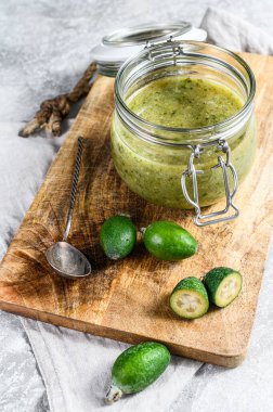 Cam kavanozdaki tahta kesme tahtasındaki yeşil fayjoa reçeli. Gri arka plan. Üst görünüm.