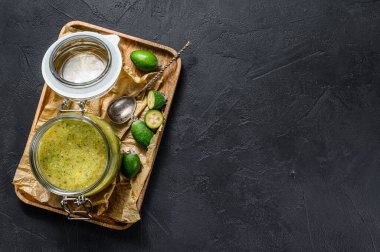 Cam kavanozdaki tahta kesme tahtasındaki yeşil fayjoa reçeli. Siyah arka plan. Üst Manzara. Metin için boşluk.