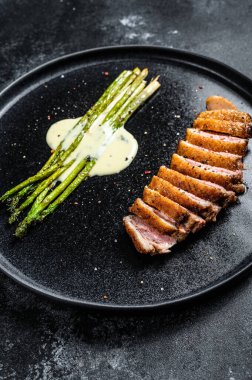 Fırında kuşkonmaz ile ızgara ördek göğsü bifteği. Siyah arka plan. Üst görünüm.