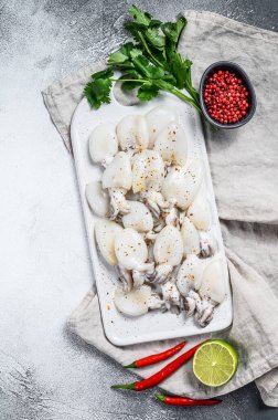 Kesme tahtasında çiğ, kırmızı biberli ve maydanozlu minyatür mürekkep balığı. Gri arka plan. Üst görünüm.