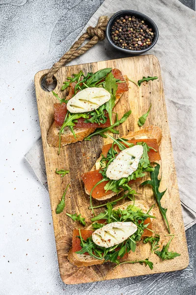 Canapes on a baguette with goat cheese, arugula and pear marmalade. Gray background. Top view.