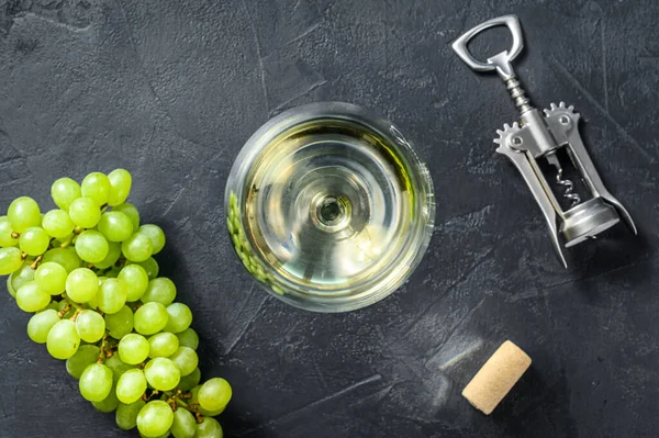 A branch of green grapes, a wine glass, a corkscrew and a cork. Concept of wine-making. Black background. Top view.