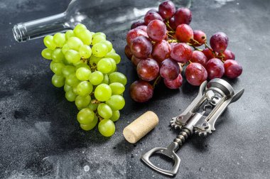 Bir dal yeşil ve kırmızı üzüm, bir şişe, bir tirbuşon ve bir mantar. Şarap yapma kavramı. Siyah arka plan. Üst görünüm.