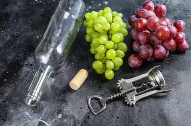 Bir dal yeşil ve kırmızı üzüm, boş bir şişe, bir tirbuşon ve bir mantar. Ev yapımı şarap kavramı. Siyah arka plan. Üst görünüm.